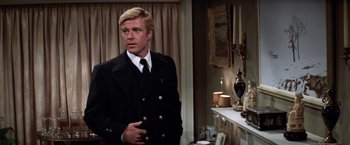 Movie still from “The Way We Were” (1973), directed by Sydney Pollack – A man wearing a suit and tie standing in a room; Medium shot, Over the shoulder angle