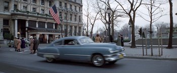 Movie still from “The Way We Were” (1973), directed by Sydney Pollack – An old car driving down a street past a tall building; Wide shot, Low angle