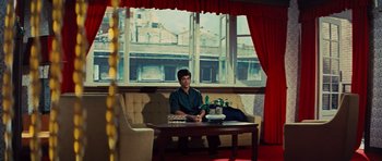 Movie still from “The Way of the Dragon” (1972), directed by Bruce Lee – A man sitting at a table in a living room; Wide shot, Low angle