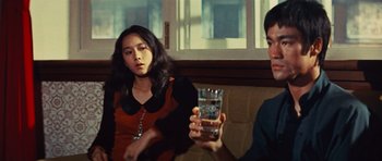 Movie still from “The Way of the Dragon” (1972), directed by Bruce Lee – A woman sitting next to a man holding a glass of water; Medium shot, Over the shoulder angle