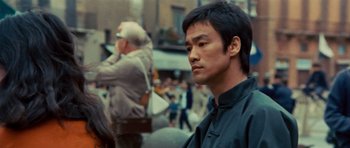 Movie still from “The Way of the Dragon” (1972), directed by Bruce Lee – A man in a black shirt is standing in the street; Close Up shot, Over the shoulder angle