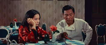 Movie still from “The Way of the Dragon” (1972), directed by Bruce Lee – An older man and a younger woman sitting at a dinner table; Medium shot, High angle