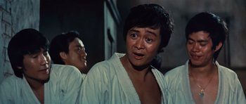 Movie still from “The Way of the Dragon” (1972), directed by Bruce Lee – A man in a white shirt is standing in front of another man; Close Up shot, Low angle