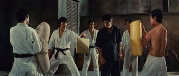 Movie still from “The Way of the Dragon” (1972), directed by Bruce Lee – A group of men in white and black martial arts outfits; Medium shot, Low angle