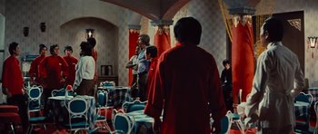 Movie still from “The Way of the Dragon” (1972), directed by Bruce Lee – A group of people standing around a room; Wide shot, Over the shoulder angle