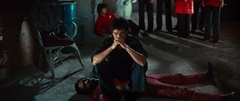 Movie still from “The Way of the Dragon” (1972), directed by Bruce Lee – A man sitting on the ground with his hands folded to his chest; Wide shot, High angle