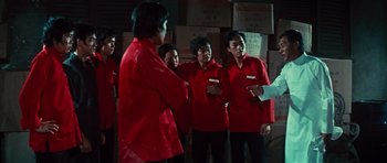 Movie still from “The Way of the Dragon” (1972), directed by Bruce Lee – A group of people in red shirts standing next to each other; Medium shot, Low angle