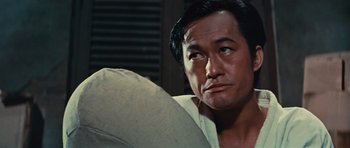 Movie still from “The Way of the Dragon” (1972), directed by Bruce Lee – An asian man looking up while sitting on a couch; Close Up shot, Low angle