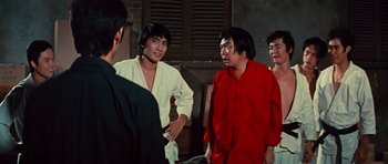 Movie still from “The Way of the Dragon” (1972), directed by Bruce Lee – A group of men standing next to each other in a room; Medium shot, Over the shoulder angle
