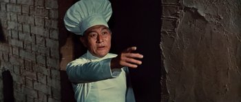 Movie still from “The Way of the Dragon” (1972), directed by Bruce Lee – A man wearing a chef's hat is pointing to the side; Medium shot, Low angle