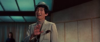 Movie still from “The Way of the Dragon” (1972), directed by Bruce Lee – A man wearing a suit and a hat is smiling; Close Up shot, Low angle