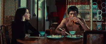 Movie still from “The Way of the Dragon” (1972), directed by Bruce Lee – A man sitting at a dinner table drinking a beer; Medium shot, Over the shoulder angle