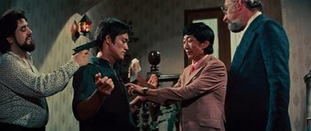 Movie still from “The Way of the Dragon” (1972), directed by Bruce Lee – Two men in a room one is wearing a suit and the other is wearing a red tie; Medium shot, Low angle