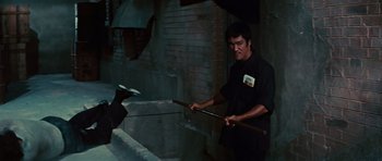 Movie still from “The Way of the Dragon” (1972), directed by Bruce Lee – A man holding a stick in his hands; Medium shot, Low angle