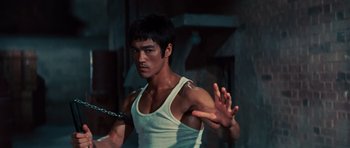Movie still from “The Way of the Dragon” (1972), directed by Bruce Lee – A man in a white tank top holding a metal chain; Medium shot, Low angle