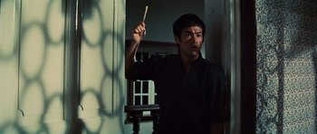 Movie still from “The Way of the Dragon” (1972), directed by Bruce Lee – A man holding a wooden stick in a room; Medium shot, Low angle