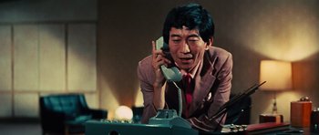 Movie still from “The Way of the Dragon” (1972), directed by Bruce Lee – A man talking on a phone while sitting at a desk; Close Up shot, Low angle