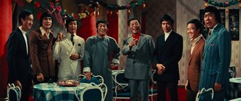 Movie still from “The Way of the Dragon” (1972), directed by Bruce Lee – A group of men standing next to each other in front of a table; Medium shot, Low angle