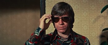 Movie still from “The Way of the Dragon” (1972), directed by Bruce Lee – A man wearing sunglasses while holding his hand up to his head; Close Up shot, Low angle