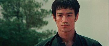 Movie still from “The Way of the Dragon” (1972), directed by Bruce Lee – A young man with short black hair wearing a black shirt; Close Up shot, Low angle