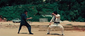 Movie still from “The Way of the Dragon” (1972), directed by Bruce Lee – Two men in suits and ties are fighting in the dirt; Wide shot, High angle