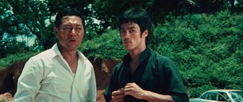 Movie still from “The Way of the Dragon” (1972), directed by Bruce Lee – A man standing next to another man on a dirt ground; Medium shot, Low angle