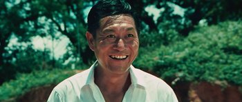 Movie still from “The Way of the Dragon” (1972), directed by Bruce Lee – An older man smiling for the camera with trees in the background; Close Up shot, Low angle