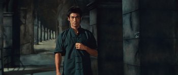 Movie still from “The Way of the Dragon” (1972), directed by Bruce Lee – A man standing in front of a stone wall holding a cell phone; Medium shot, Low angle