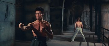 Movie still from “The Way of the Dragon” (1972), directed by Bruce Lee – A man standing next to another man in a dark room; Medium shot, Low angle