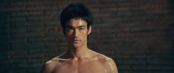 Movie still from “The Way of the Dragon” (1972), directed by Bruce Lee – A shirtless man with a brick wall in the background; Close Up shot, Low angle