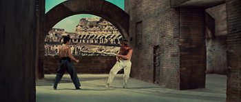 Movie still from “The Way of the Dragon” (1972), directed by Bruce Lee – A man in white pants and a shirt is in front of an archway; Wide shot, Low angle