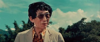 Movie still from “The Way of the Dragon” (1972), directed by Bruce Lee – An older man wearing a suit and sun glasses; Close Up shot, Low angle