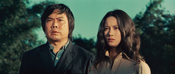Movie still from “The Way of the Dragon” (1972), directed by Bruce Lee – A man and a woman standing next to each other in front of trees; Medium shot, Low angle