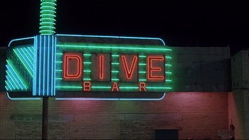Movie still from “The Way of the Gun” (2000), directed by Christopher McQuarrie – A neon dive bar sign lit up at night; Wide shot, Low angle
