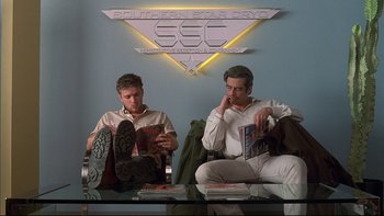 Movie still from “The Way of the Gun” (2000), directed by Christopher McQuarrie – A couple of men sitting next to each other on a table; Wide shot, Low angle