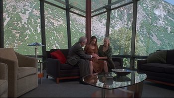 Movie still from “The Way of the Gun” (2000), directed by Christopher McQuarrie – A man and two women sitting on a couch in front of a window; Wide shot, High angle
