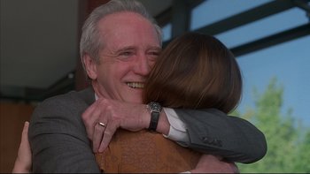 Movie still from “The Way of the Gun” (2000), directed by Christopher McQuarrie – An older man hugging a younger woman in a gray suit; Close Up shot, Over the shoulder angle