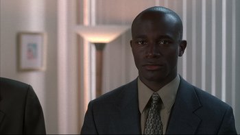 Movie still from “The Way of the Gun” (2000), directed by Christopher McQuarrie – A man in a suit and tie standing in front of a wall; Close Up shot, Low angle