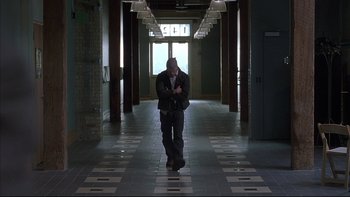 Movie still from “The Way of the Gun” (2000), directed by Christopher McQuarrie – A man walking down a hallway in a building; Wide shot, Low angle