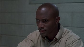 Movie still from “The Way of the Gun” (2000), directed by Christopher McQuarrie – A man with a bald head sitting in front of a brick wall; Close Up shot, High angle