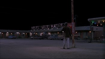 Movie still from “The Way of the Gun” (2000), directed by Christopher McQuarrie – A man standing in a parking lot next to a pole; Wide shot, Low angle