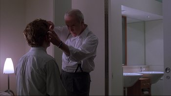 Movie still from “The Way of the Gun” (2000), directed by Christopher McQuarrie – An older man is putting on a young man's hair; Medium shot, Over the shoulder angle