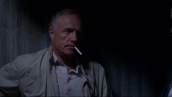 Movie still from “The Way of the Gun” (2000), directed by Christopher McQuarrie – An older man smoking a cigarette in a dark room; Close Up shot, Low angle