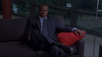 Movie still from “The Way of the Gun” (2000), directed by Christopher McQuarrie – A man in a suit sitting on a couch; Medium shot, Low angle