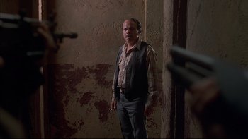 Movie still from “The Way of the Gun” (2000), directed by Christopher McQuarrie – A man standing in front of a brick wall; Medium shot, Over the shoulder angle