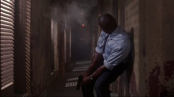 Movie still from “The Way of the Gun” (2000), directed by Christopher McQuarrie – A man sitting on a wall in a dark alley; Medium shot, Low angle