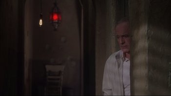 Movie still from “The Way of the Gun” (2000), directed by Christopher McQuarrie – A man standing in a room with a red light hanging from the ceiling; Medium shot, Low angle