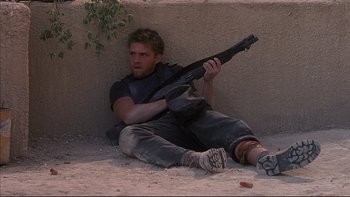 Movie still from “The Way of the Gun” (2000), directed by Christopher McQuarrie – A man sitting on the ground holding a gun; Medium shot, High angle