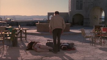 Movie still from “The Way of the Gun” (2000), directed by Christopher McQuarrie – A man standing in the sand next to a group of people laying on the ground; Wide shot, Low angle