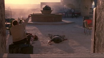 Movie still from “The Way of the Gun” (2000), directed by Christopher McQuarrie – A man laying on the ground in the middle of the day; Wide shot, Over the shoulder angle